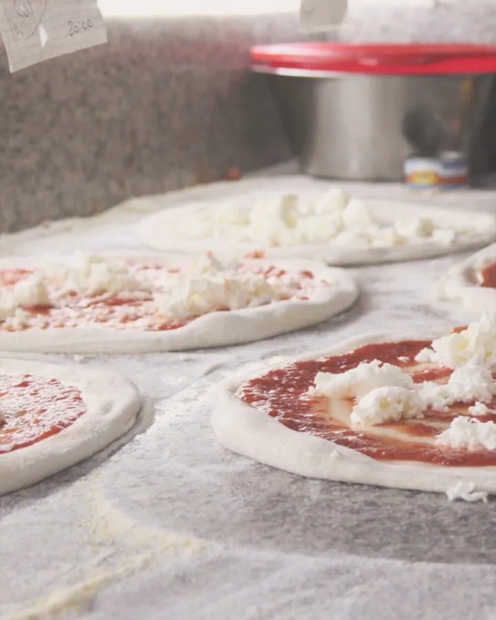 Pizze stese sul banco, con pomodoro e mozzarella, pronte per il forno