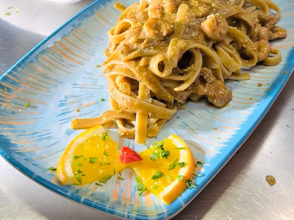 Un piatto di pasta con gamberi e pistacchio, con spicchi d'arancia, su un vassoio azzurro