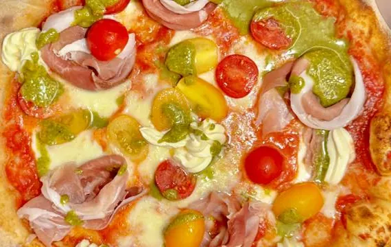 Una pizza vista dall'alto con prosciutto crudo, pomodorini rossi e gialli e pesto